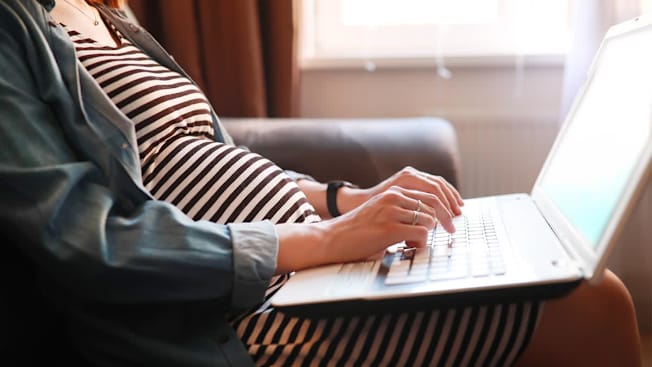 Pregnant person sitting on a couch using a laptop.