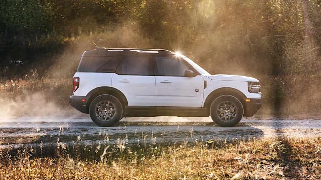2026 Ford Bronco Sport seen driving on a dirt road in a forested environment.