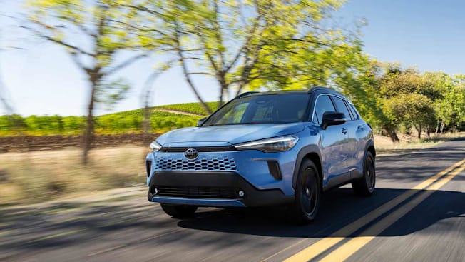 2026 Toyota Corolla Cross Hybrid driving on a two lane road with trees.