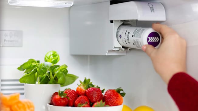 A hand installing a Whirlpool Everydrop filter  into a refrigerator filled with produce.