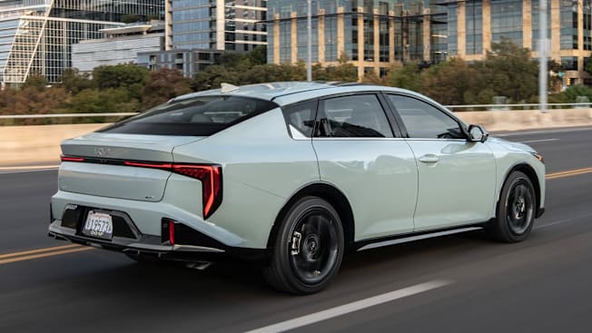 light blue Kia K4 on elevated road with city skyscrapers in background