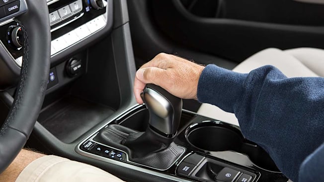 A hand holding the gear shift of an automatic car.