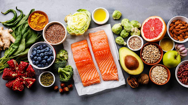 overhead view of various fruits, vegetables, grains, nuts, and salmon on grey background