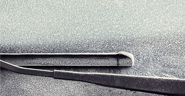 Closeup of windshield wiper blades on a frosty car windshield.