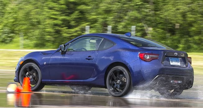 blue car on wet road driving between orange safety cones