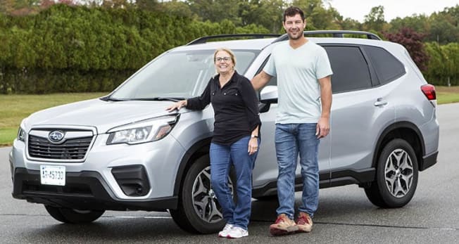 a tall and a short person both standing next to a Subaru Forester
