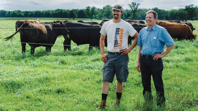 Duane Munsterteiger and his son standing in field with cows in the background.