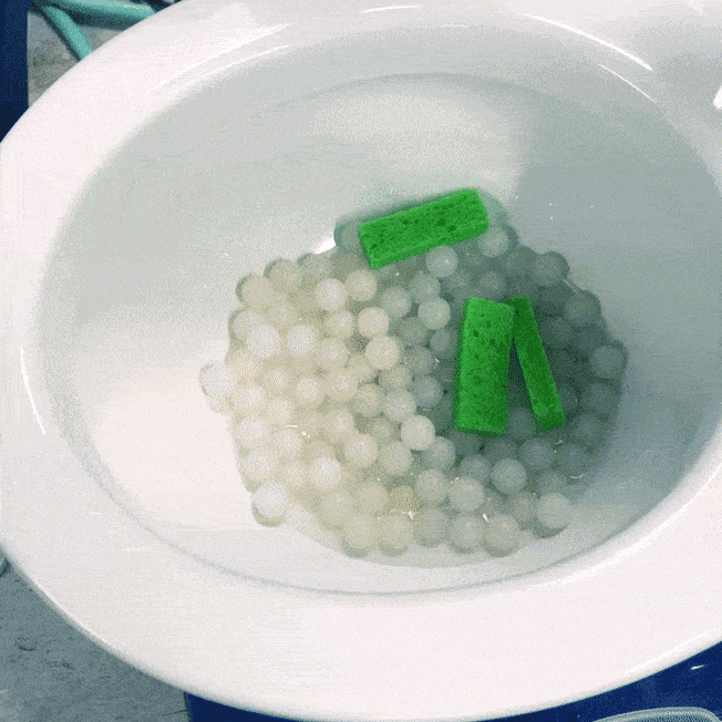 toilet being flushed with sponges, water filled condom, and white plastic balls