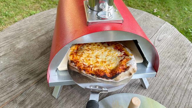 A finished pizza being slid out of the Le Peppe pizza oven on a metal pizza peel
