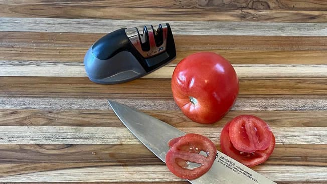 KitchenIQ knife sharpener seen on a cutting board with a knife and cut tomato.