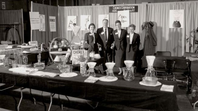 black and white photo of group of people in lab fair with coffee makers on tables in front of them