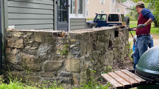 Mason workers break down stone wall.
