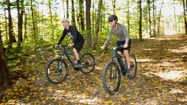 people riding Trek Powerfly 4 and Giant Talon E+ electric mountain bikes through wooded area