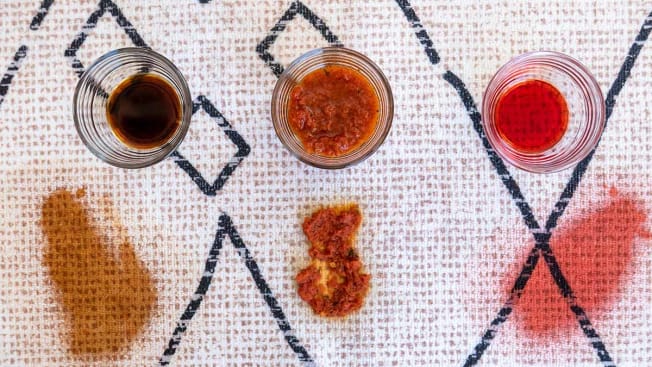three small bowls of sauces with sauce stains on a white rug