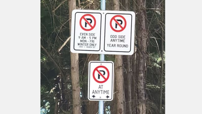three different parking signs with different parking regulations and trees in background