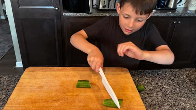 a boy learning to cut cucumbers with a child safety knife