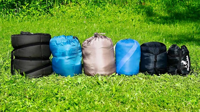 Six sleeping bags in stuff sacks on grass