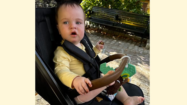 baby in Nuna TRVL LX stroller holding food with food covering hand and mouth