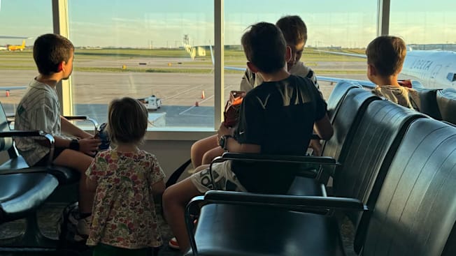 5 children sitting at an airport looking outside