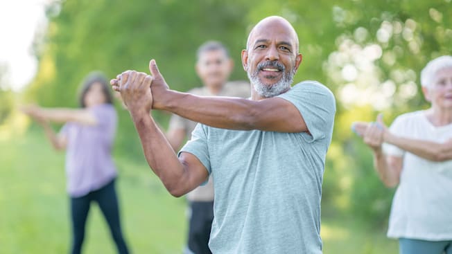 person doing tai chi outside with 3 people and trees blurred in the background