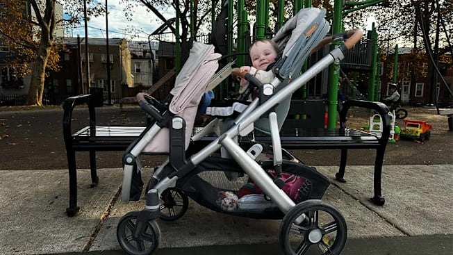 A Bugaboo Vista stroller parked in a playground with a happy baby sitting inside.
