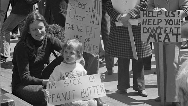 A gathering of people protesting the price of meat with one child holding a sign saying "I'm sick of peanut butter".
