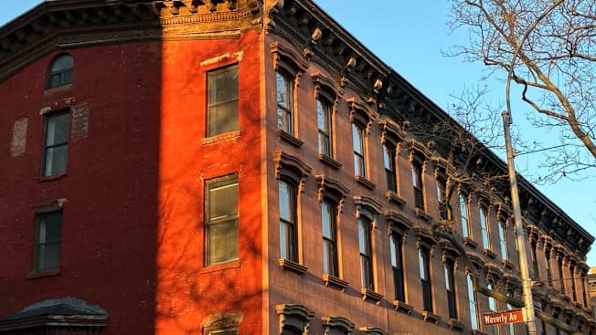brick apartment building with sunset light casting on side of building with street sign and tree