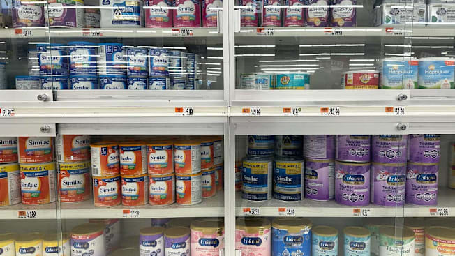 A locked case at a grocery store displaying containers of various powdered formula brands.
