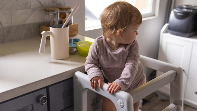 A toddler standing in a kitchen toddler tower at a kitchen counter.