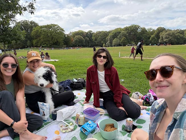 A selfie of a group of friends and dog having a picnic in a park.