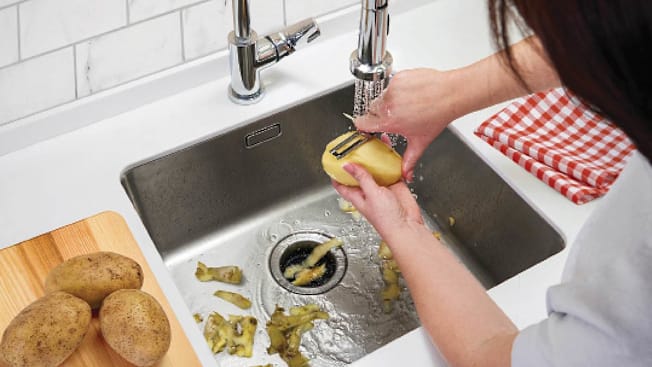 A photo illustration showing a woman peeling a potato and letting the skins go down a disposal.