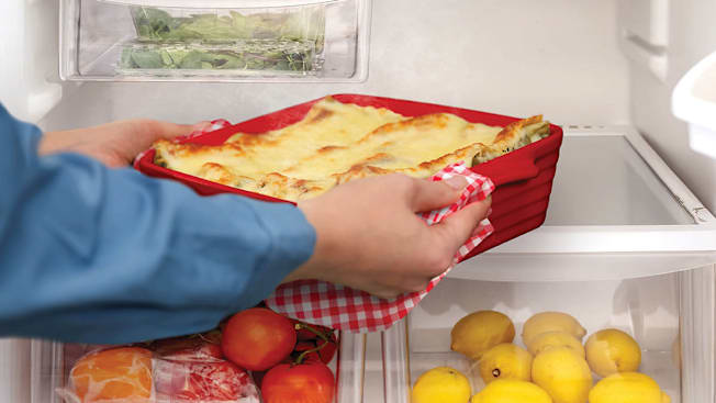A photo illustration showing a person placing a hot dish into a cold refrigerator.