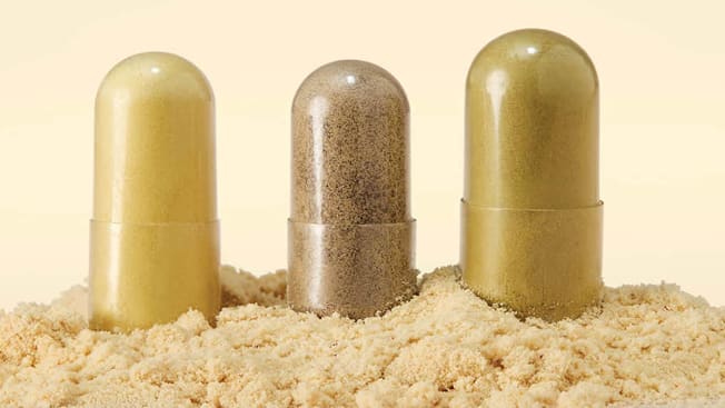 Three supplement pills sitting in a pile of protein powder