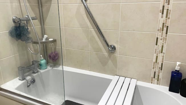 A home bathroom showing a bench placed across the bathtub and a grab bar.