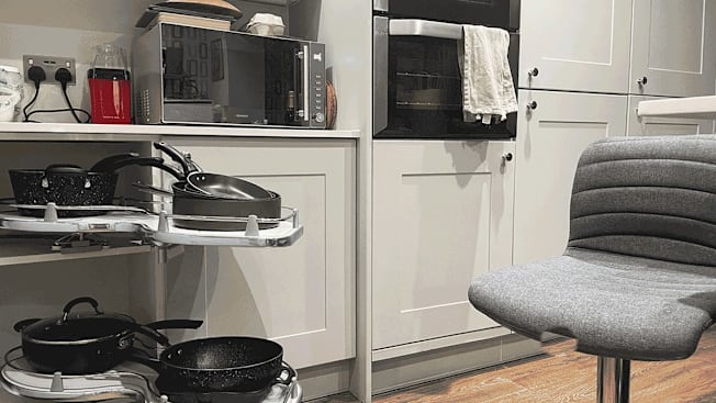 The interior of a home kitchen showing pull-out shelving with pots and pans, a wall oven, and a chair.