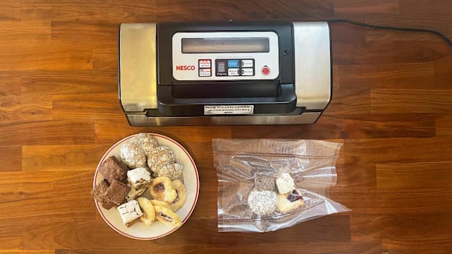 An overhead view of a vacuum sealer with a plate of cookies and a bag of vacuum sealed cookies on a wooden kitchen counter.