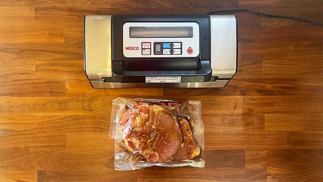 An overhead view of a vacuum sealer with a  bag of vacuum sealed pork on a wooden kitchen counter.