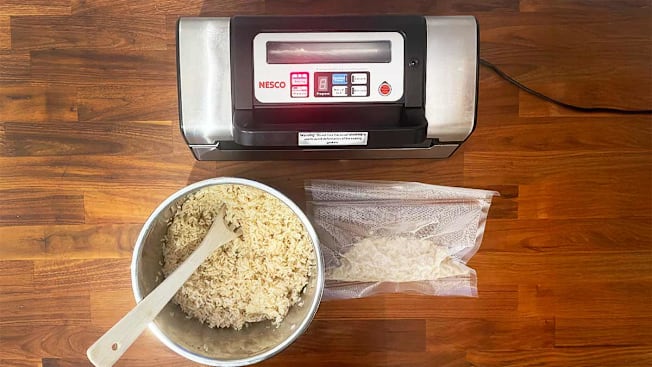 An overhead view of a vacuum sealer with a bowl of brown rice and a bag of vacuum sealed brown rice on a wooden kitchen counter.