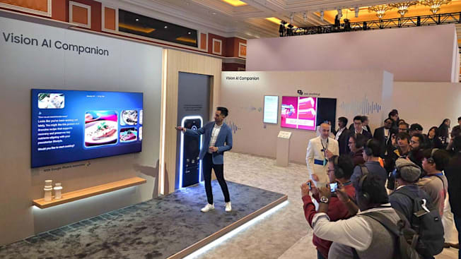 person presenting Samsung Vision AI Comparison on TV screen with crowd of people documenting the presentation