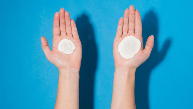 Two open hands held side by side against a blue background, each holding a dollop of sunscreen, comparing different amounts.