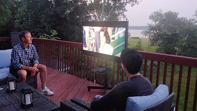 Jim Willcox seated on a deck in the evening watching TV.