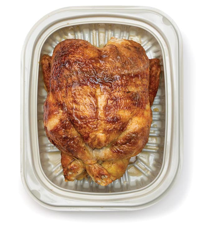 A whole rotisserie chicken with golden-brown skin sits in a white plastic takeout container.