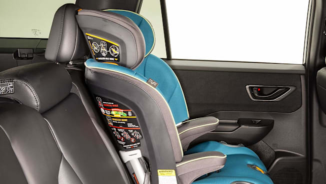 A car seat installed in the rear left seat of a vehicle. The top of the car seat is bumping up against the seat's headrest.
