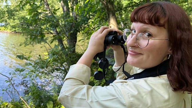 A tester holding Nikon Monarch M7 8x42 binoculars in an outdoor setting.