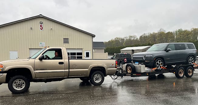 Rivian R1S shipped via pickup truck pulling a car trailer.