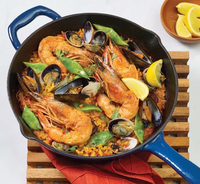 A blue cast iron skillet filled with seafood paella on a wooden hot plate.