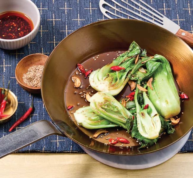 Stir-fried bok choy with garlic, chilies, and sesame seeds in a seasoned pan carbon steel pan.