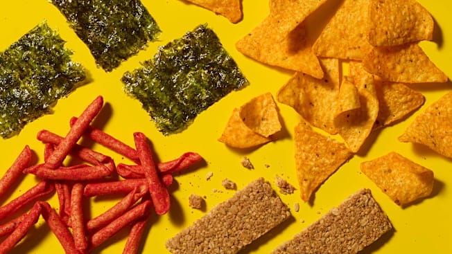 Nature Valley Crunchy Granola Bars Oats 'n Honey, Doritos Nacho Cheese Tortilla Chips, Takis Fuego Rolled Tortilla Chips, and Gimme Roasted Seaweed Snacks Sea Salt arranged on a bright yellow background.