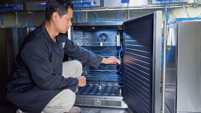 Kyaw Naing placing a thermocoupler in an outdoor refrigerator in a testing lab at Consumer Reports.