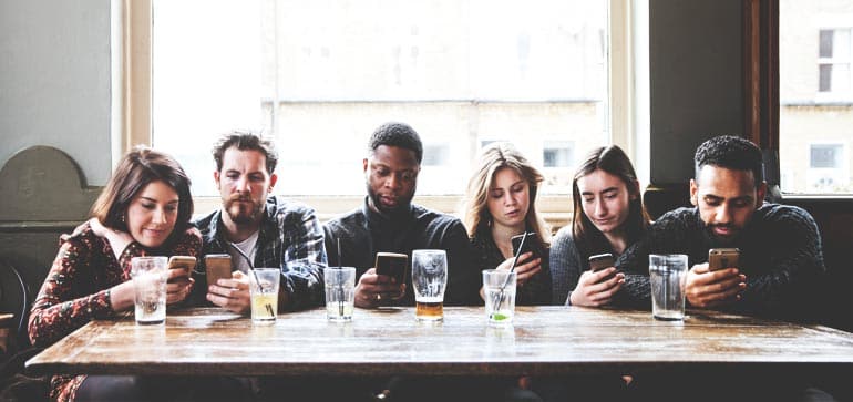 A group of friends on their phones in a bar, possibly choosing among cell-phone companies